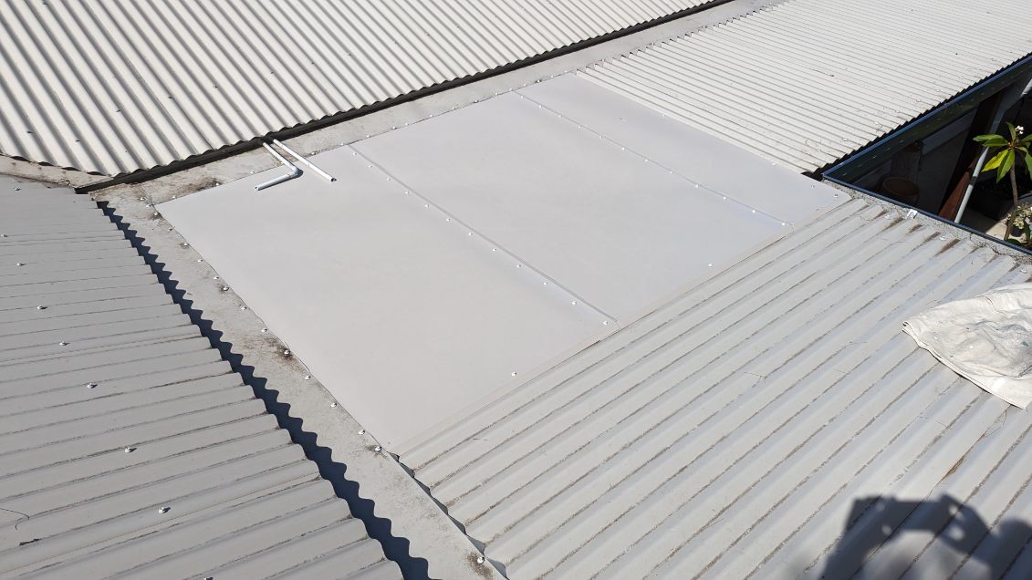 A new flat metal patch panel fixed into a corrugated roof where two roof sections meet