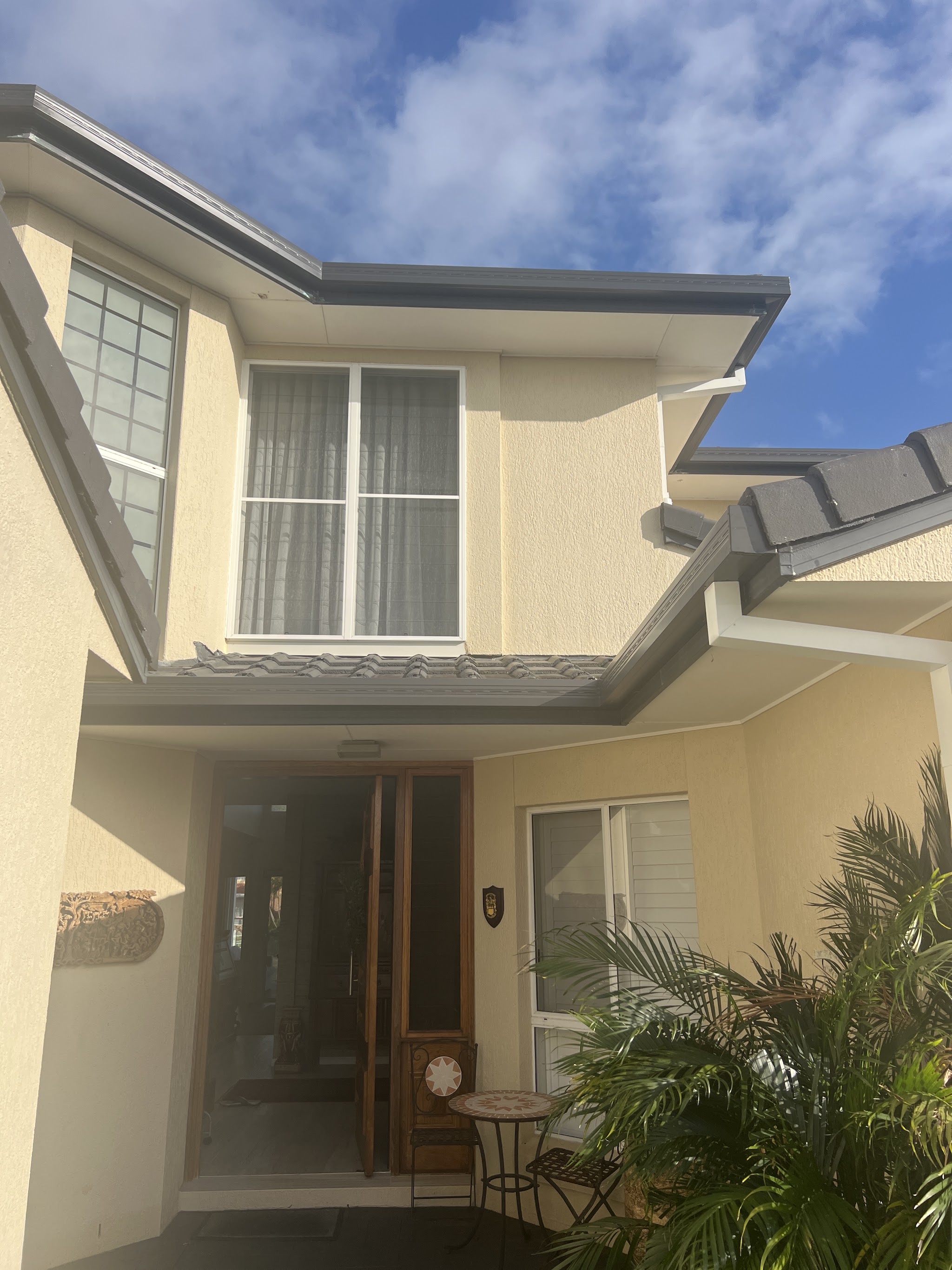 The entrance of a cream rendered two-storey home with dark gutters and fascia along both roof lines